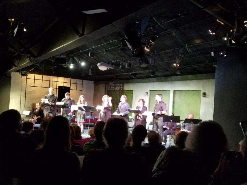 Audience watching 7 actors standing at music stands during a scene.