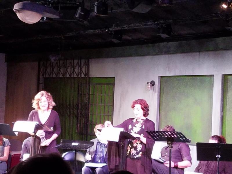 2 actors standing at music stands with scripts presenting a scene.