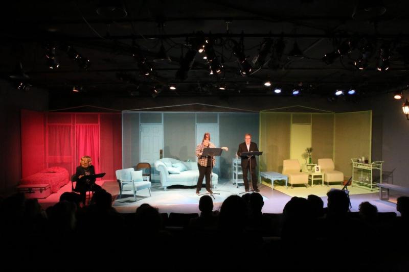 Audience view of seated woman and two actors onstage during play reading.