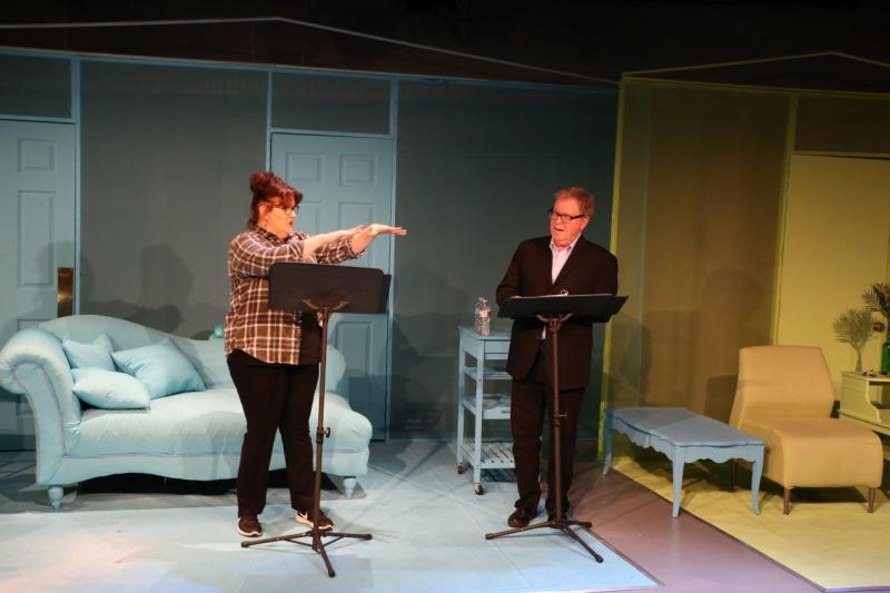 Woman in brown checked shirt gesturing with both hands at man in brown suit.