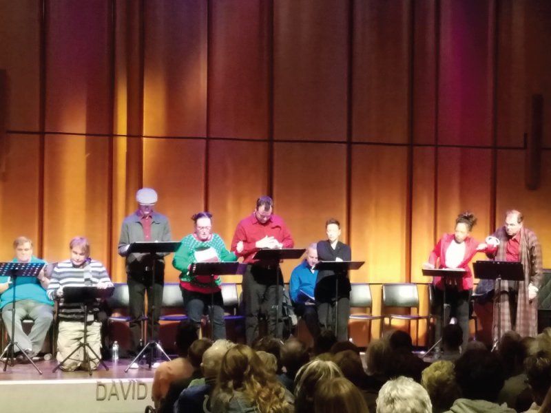 Actors on stage at music stands or seated in front of audience.