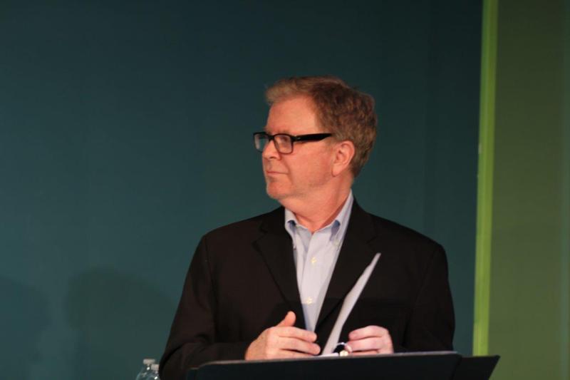 Close-up of profile of man in brown suit standing at music stand.