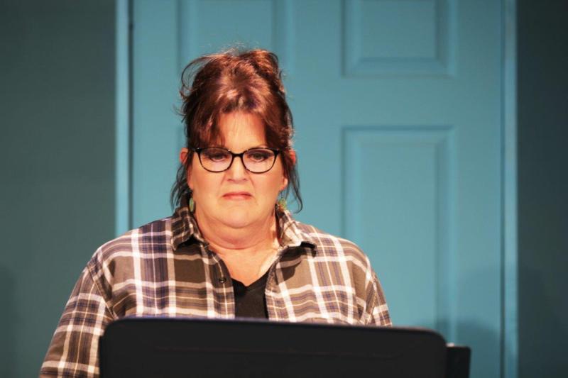 Close-up of woman in brown checked shirt and glasses standing at music stand.