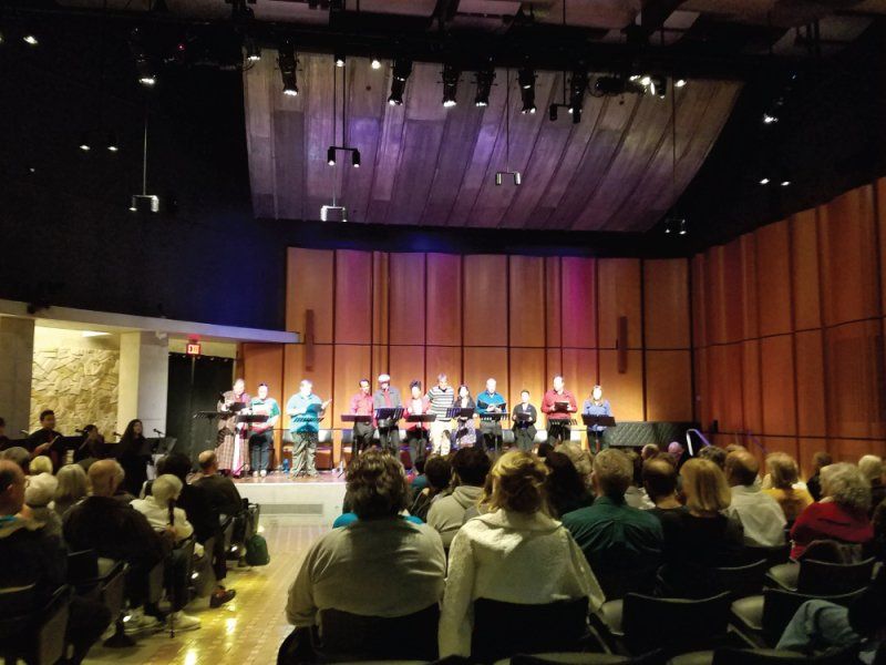 Many actors on stage at music stands during play reading at San Diego Main Library.