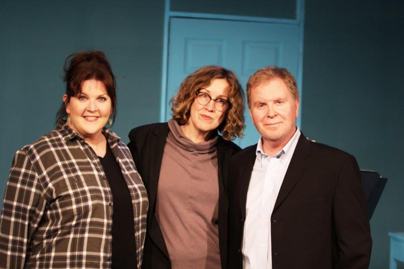 Woman in brown checked shirt, woman in brown sweater, and man in brown suit on stage.