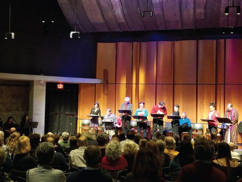 Side view of actors on stage at music stands or seated during reading at Neil Morgan Auditorium.
