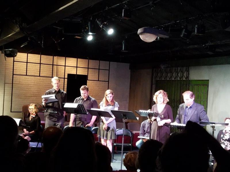 Two men, two women and one man standing at music stands during a scene.