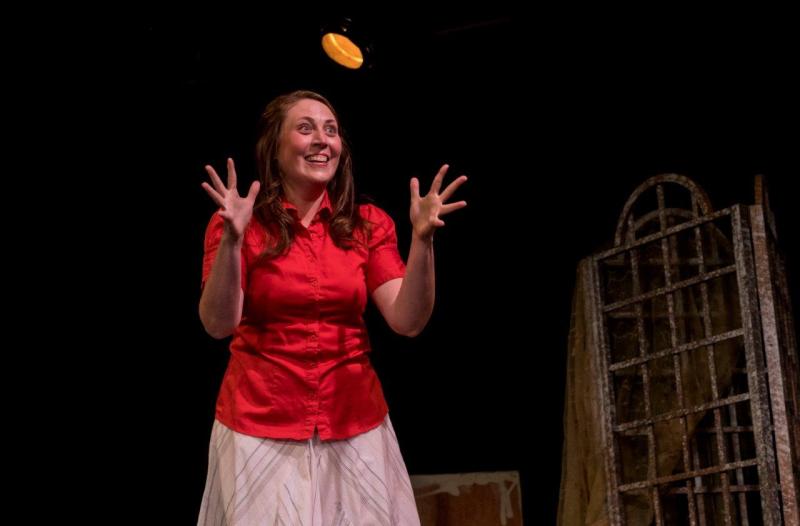 Woman in red blouse with both hands up acting out a scene  on stage.