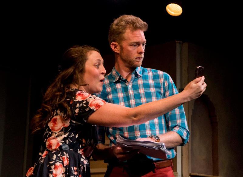 Woman in flowered blouse showing a cellphone to man in blue checked shirt .