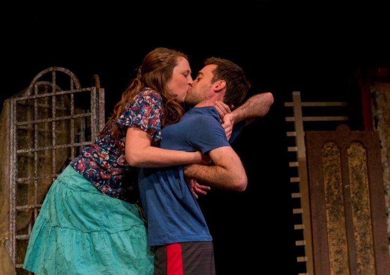 Woman in flowered blouse kissing man in blue t-shirt while rehearsing.