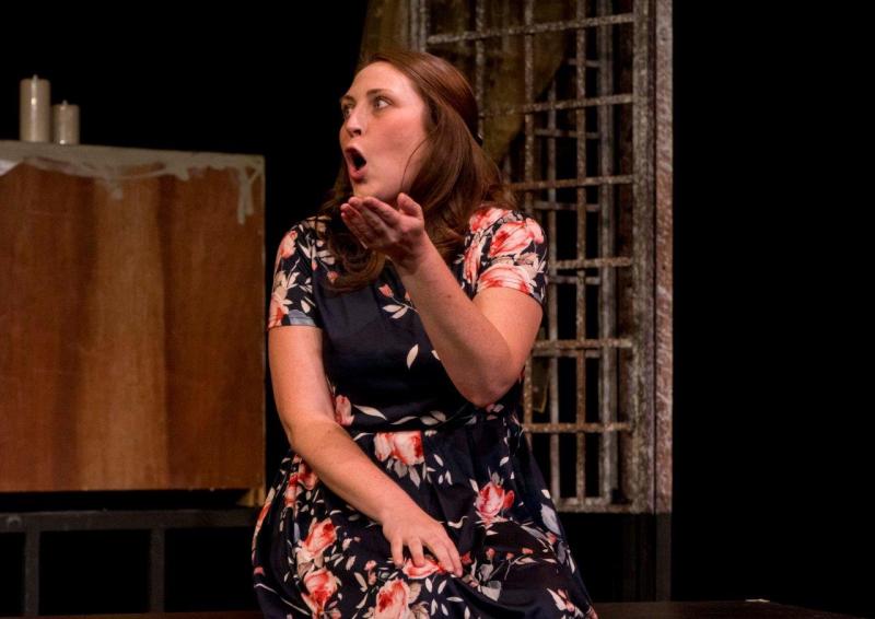 Woman in flowered dress telling a story while seated on bench on stage.