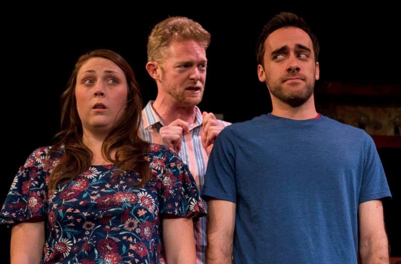 Woman in flowered dress and man in blue t-shirt listening to man in striped shirt.