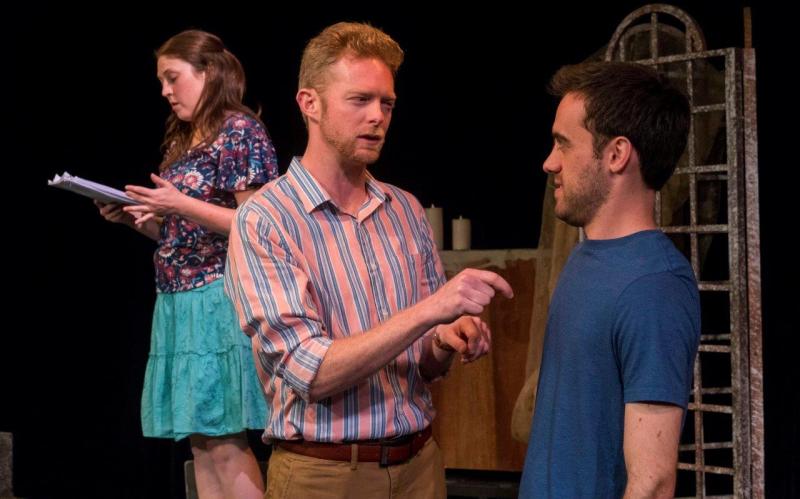 Woman in flowered blouse upstage of man in striped shirt and man in blue t-shirt.