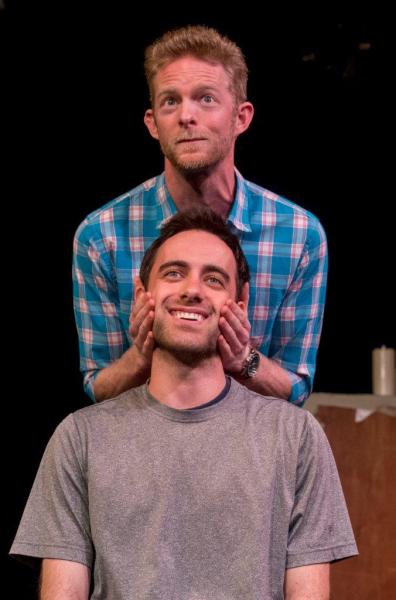 Man standing in blue checked shirt showing acting exercises to seated man in grey shirt .