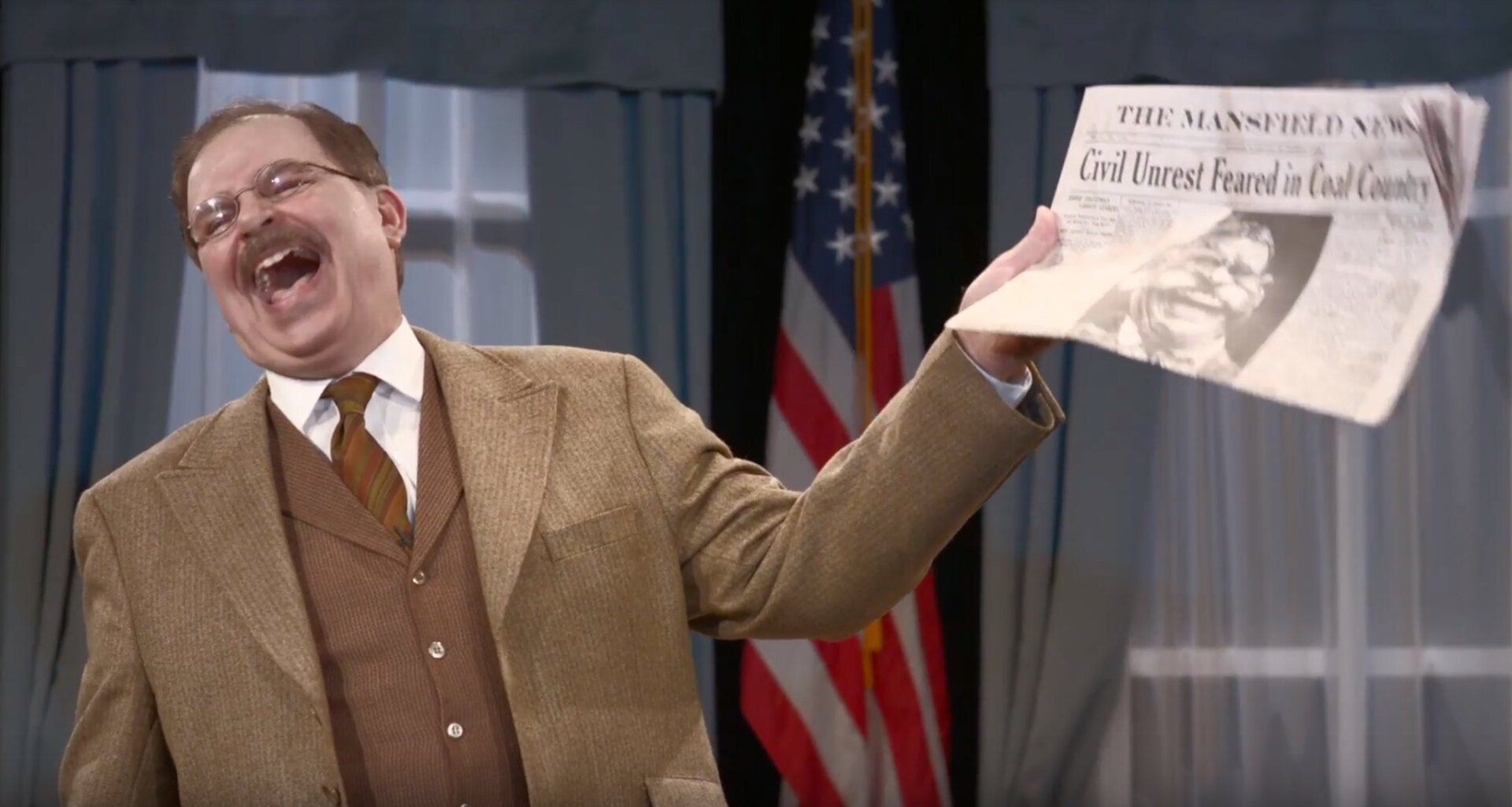 Actor Phil Johnson as President T. Roosevelt waving newspaper and laughing
