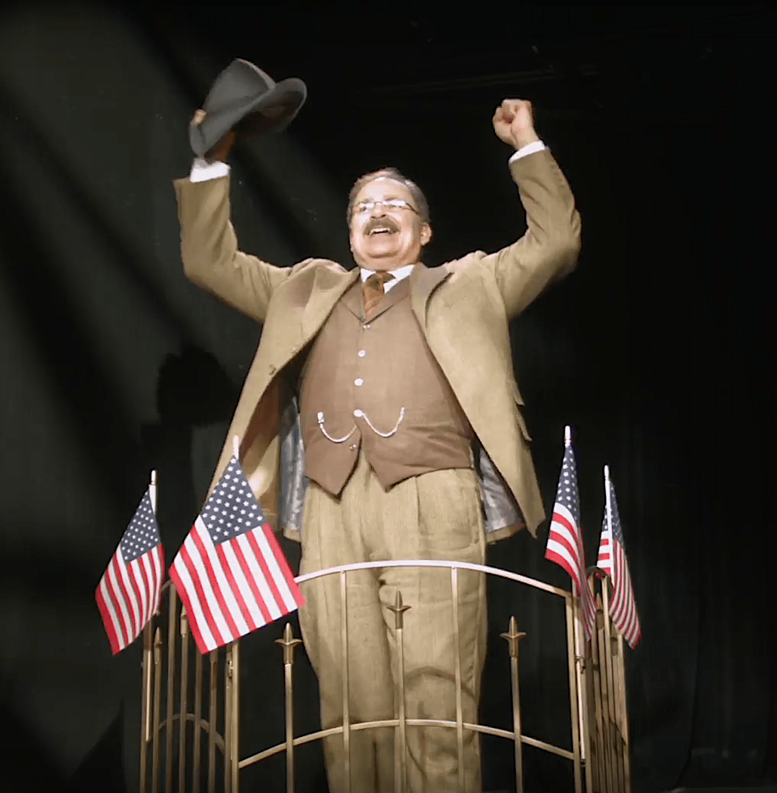 Actor Phil Johnson as President T. Roosevelt standing  on a train car surrounded by American flags