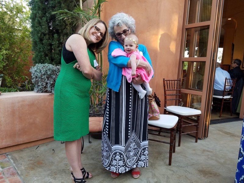 1 woman in green dress and one woman in black and white dress holding a baby.