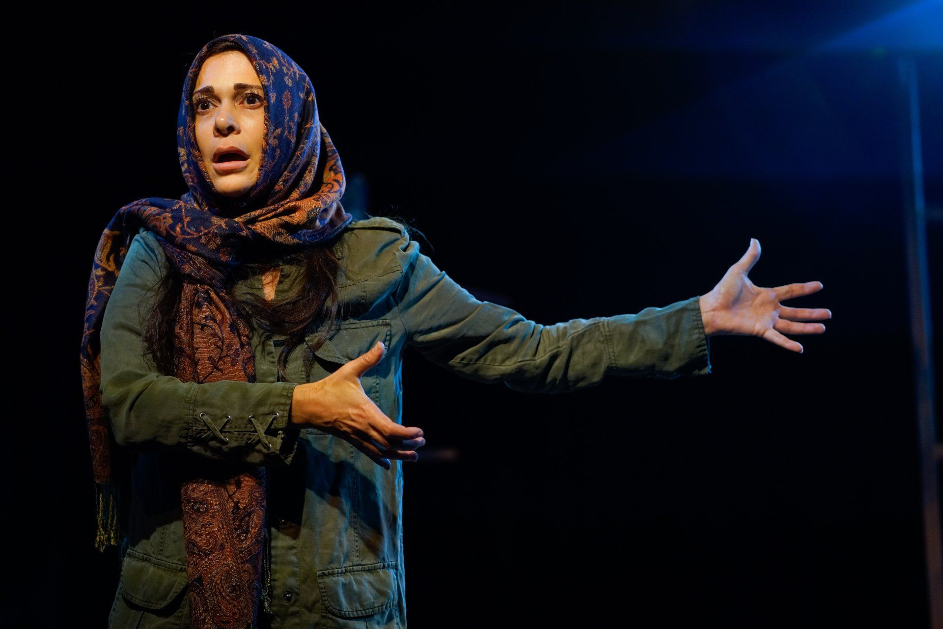 Young Mahshid wearing scarf and green jacket with hands gesturing to the left.
