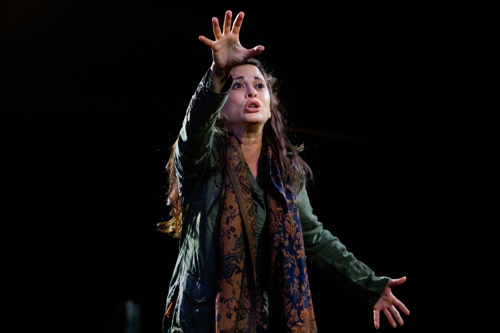 Young Mahshid wearing scarf and green jacket with her right hand in air.