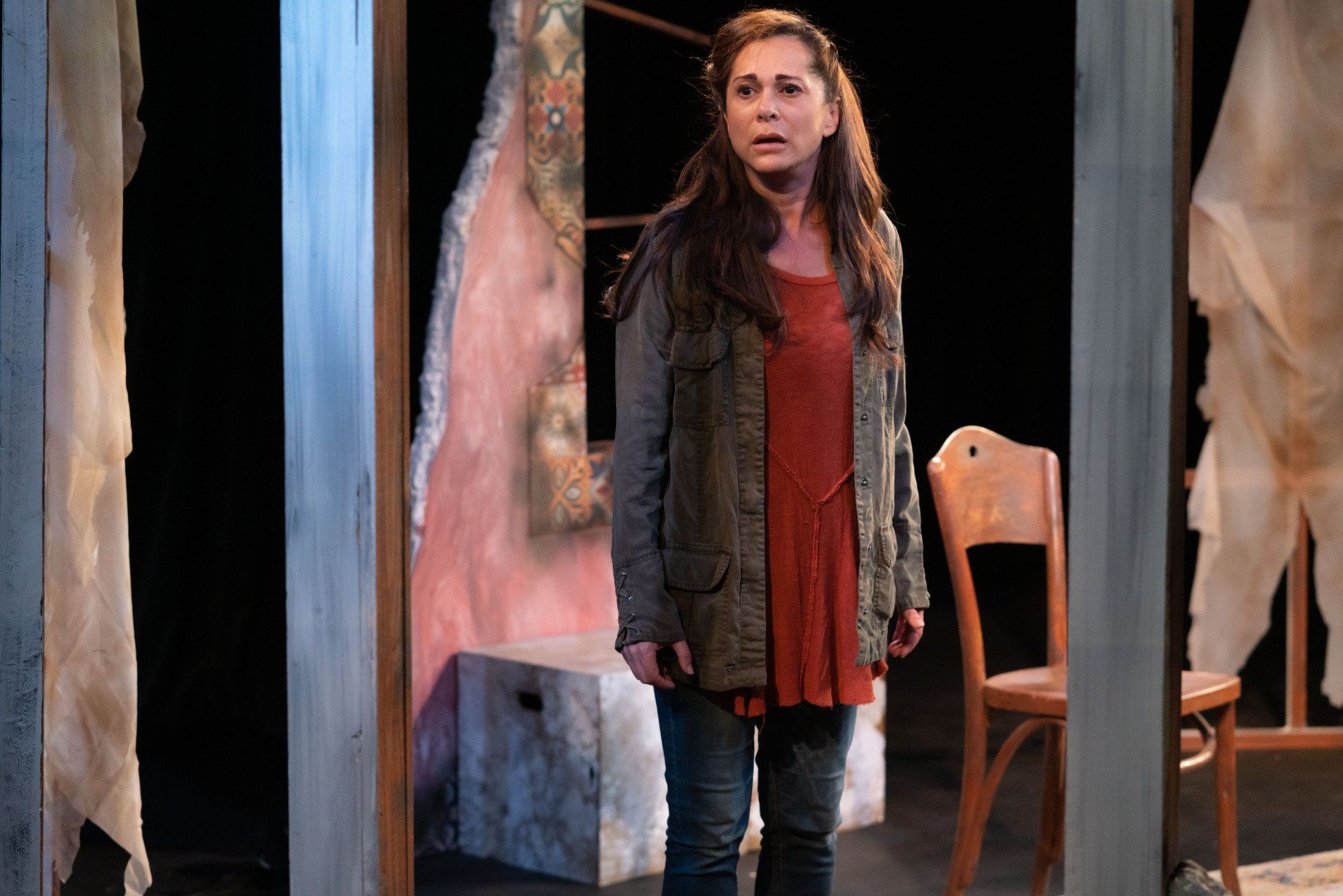 Young Mahshid wearing orange sweater and green jacket and a worried look on her face.