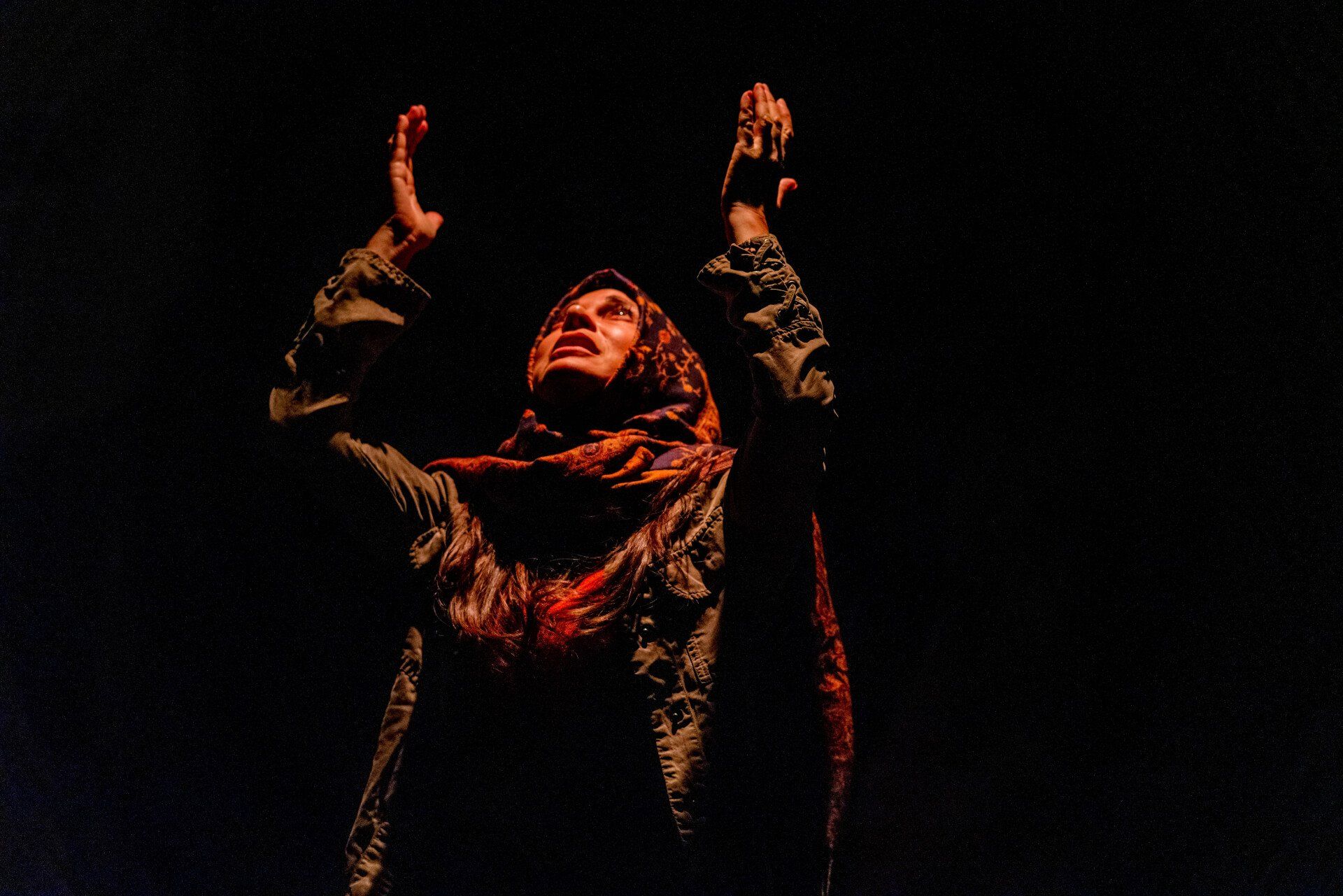 Young Mahshid in semi-darkness raising her hands in the air.
