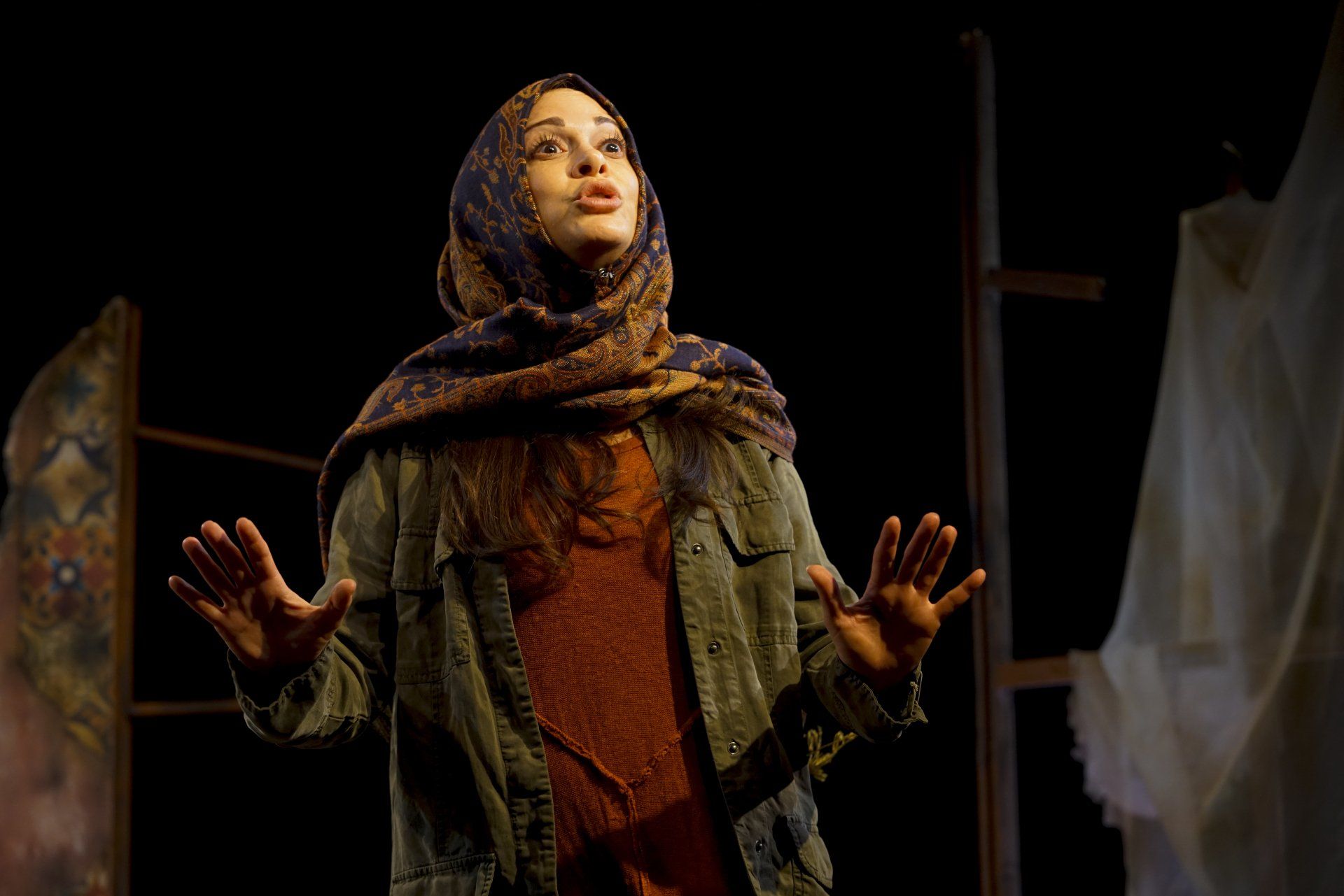 Young Mahshid wearing headscarf, orange sweater, and green jacket telling a story.