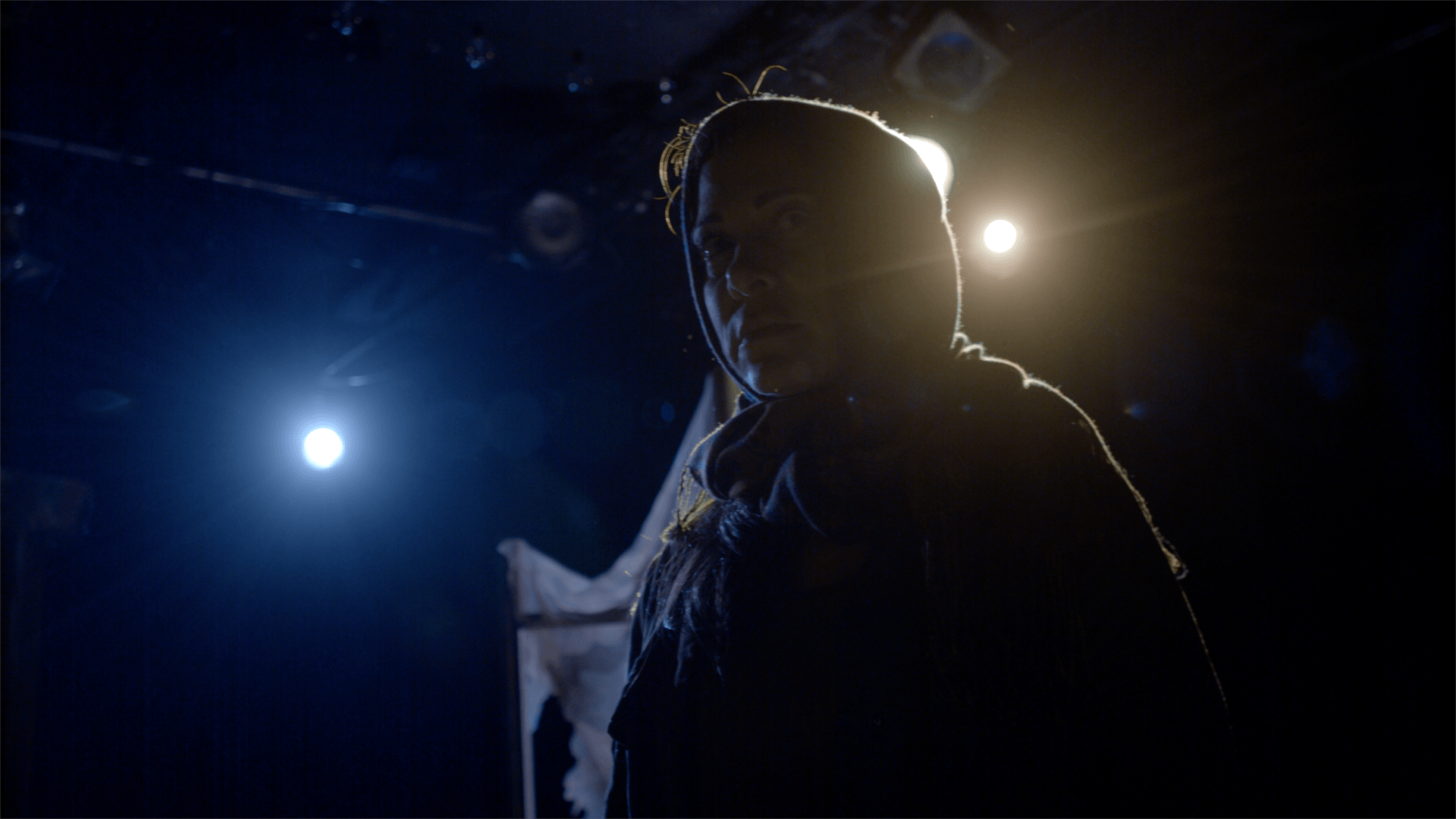 Young Mahshid in semi-darkness with lights shining from behind.