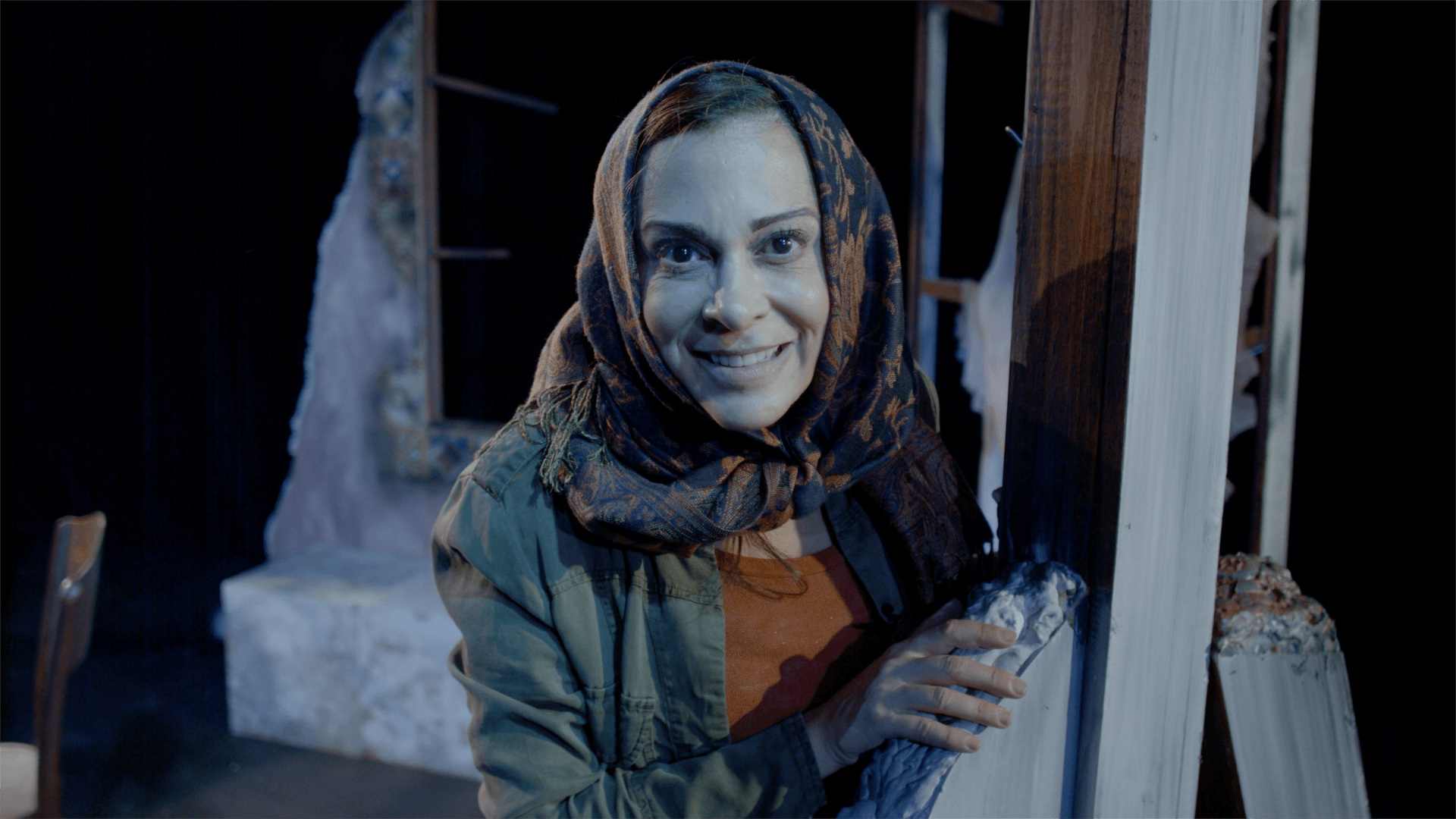 Close-up of Young Mahshid, smiling, wearing headscarf, orange sweater and headscarf.