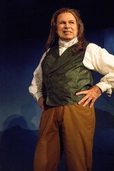 Man in long black wig and black vest considering his options.