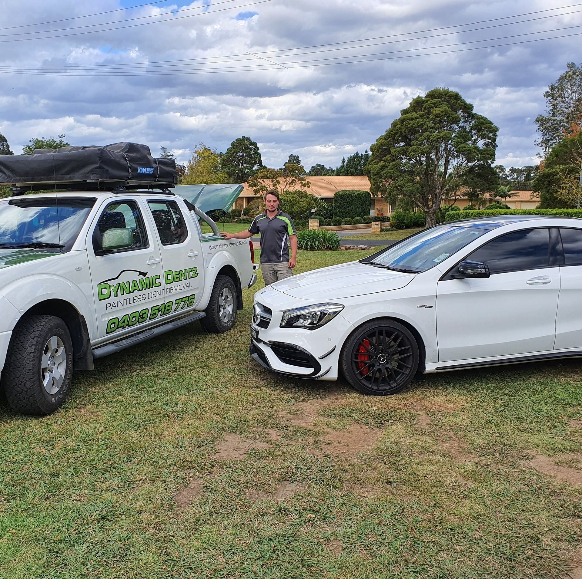 A man is standing next to two white cars in a grassy field — Dynamic Dentz Smash Repair in South Nowra, NSW
