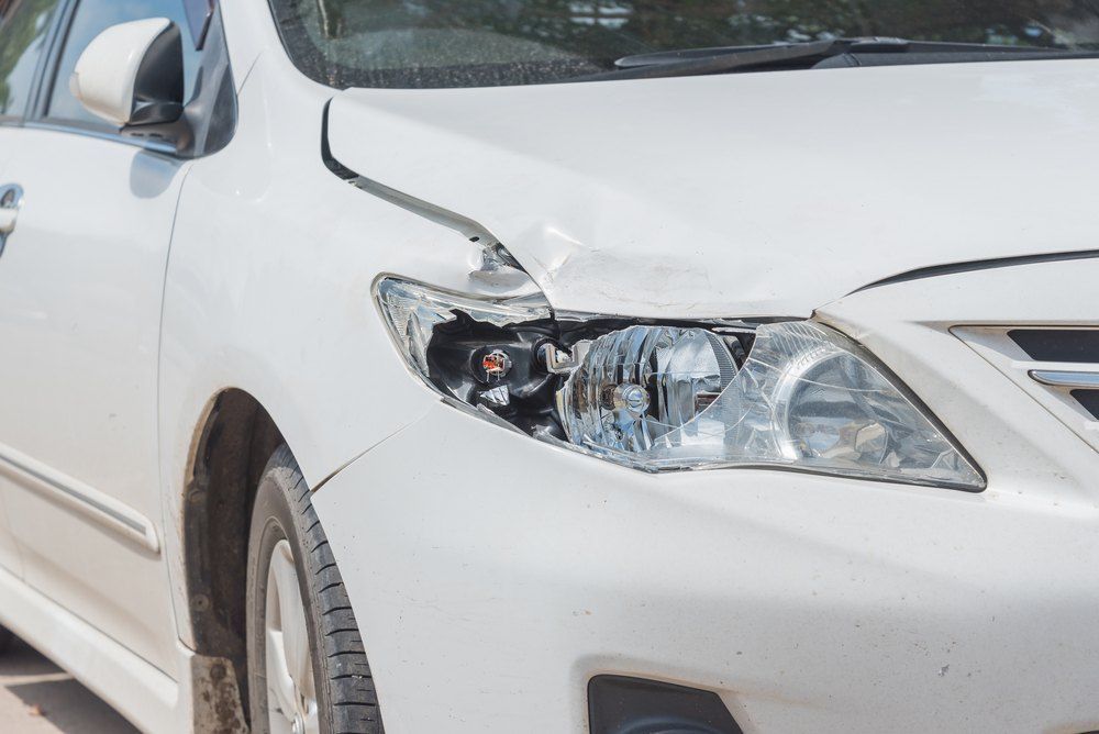 A White Car With a Damaged Headlight is Parked on the Side of the Road — Dynamic Dentz Smash Repair in North Nowra, NSW