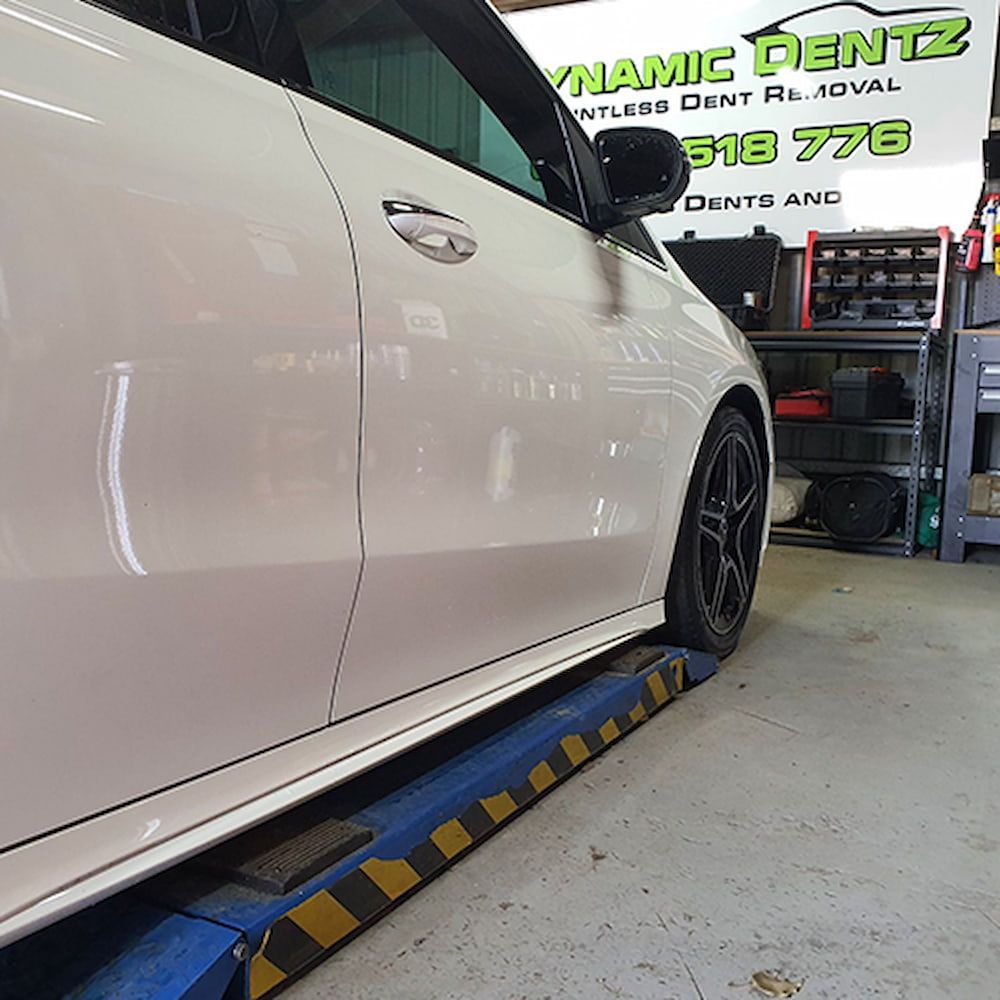 A White Car is Sitting on a Lift in a Garage — Dynamic Dentz Smash Repair in South Nowra, NSW