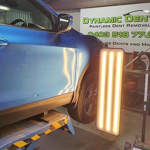 A Blue Car is Sitting on a Lift in a Garage Next to a Light — Dynamic Dentz Smash Repair in South Nowra, NSW