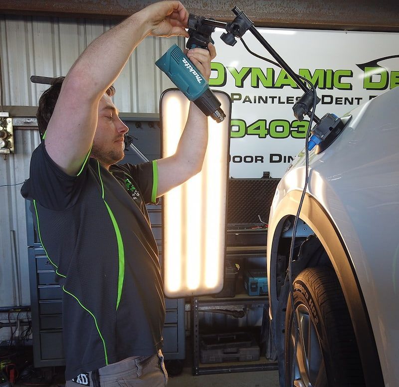 A Man is Working on a Car in Front of a Dynamic Dent Sign — Dynamic Dentz Smash Repair in South Nowra, NSW