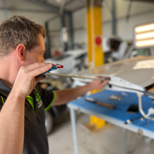A man is holding a screwdriver in his mouth in a garage — Dynamic Dentz Smash Repair in South Nowra, NSW