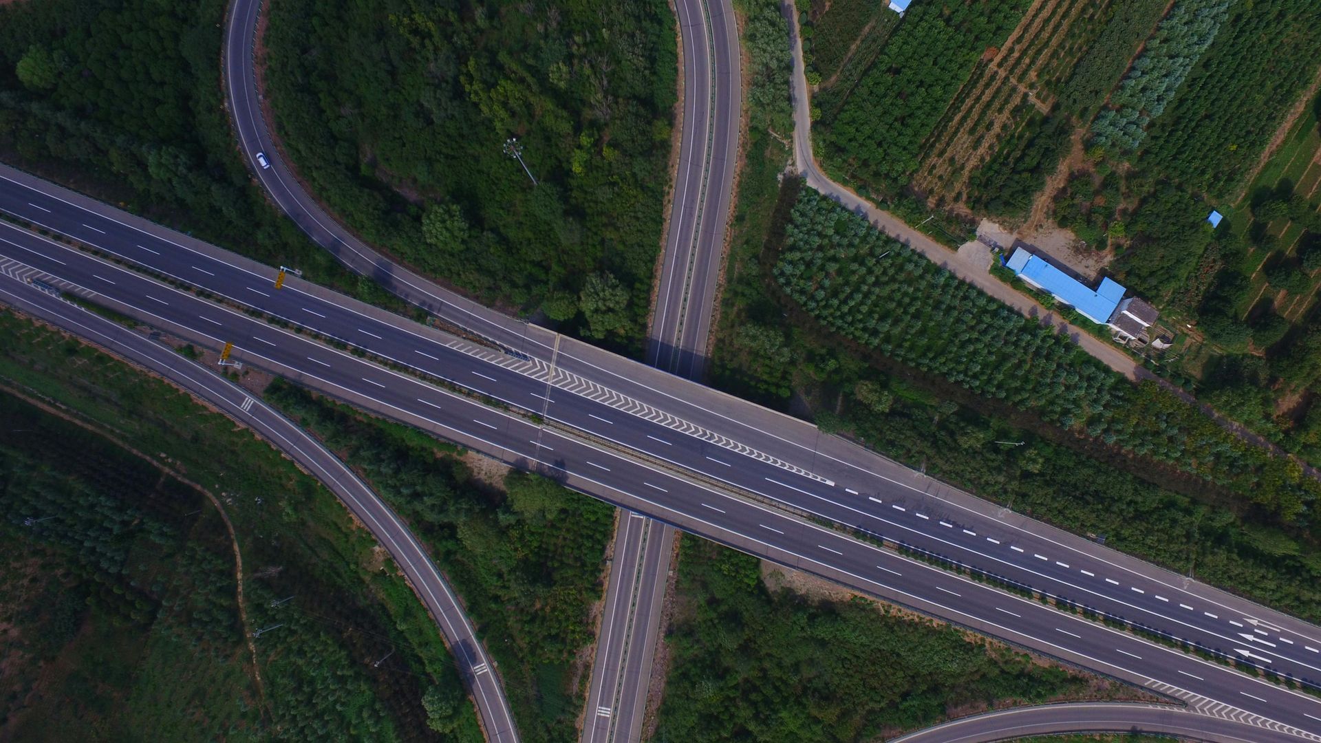 Aerial view of a highway interchange with overpasses crossing through a green wooded area.