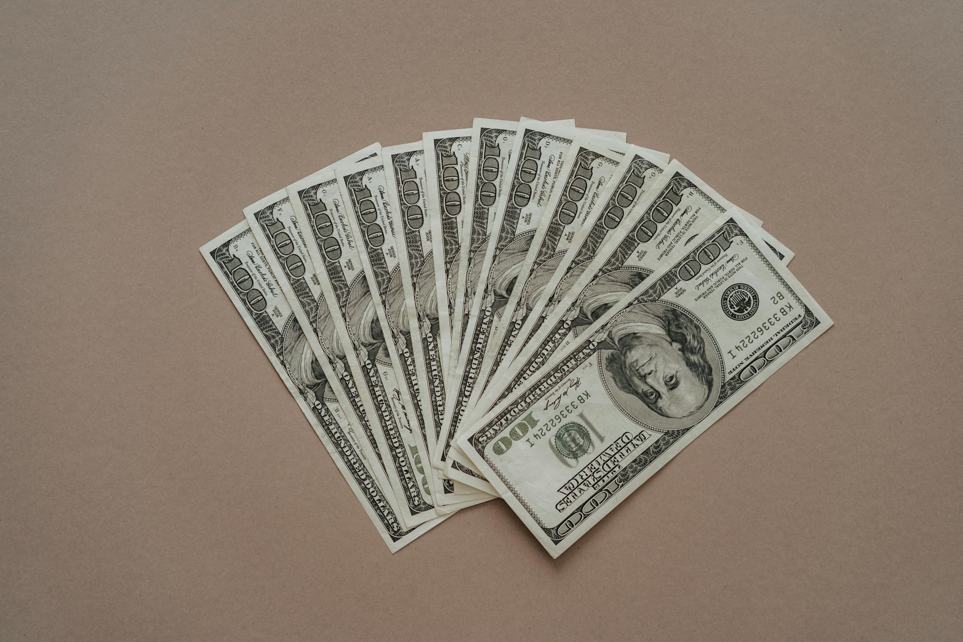 Fan of US $100 bills on a tan surface.