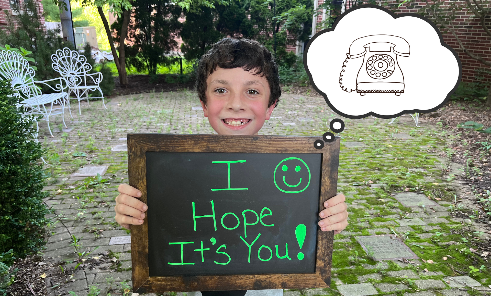 A smiling boy holds a chalkboard reading