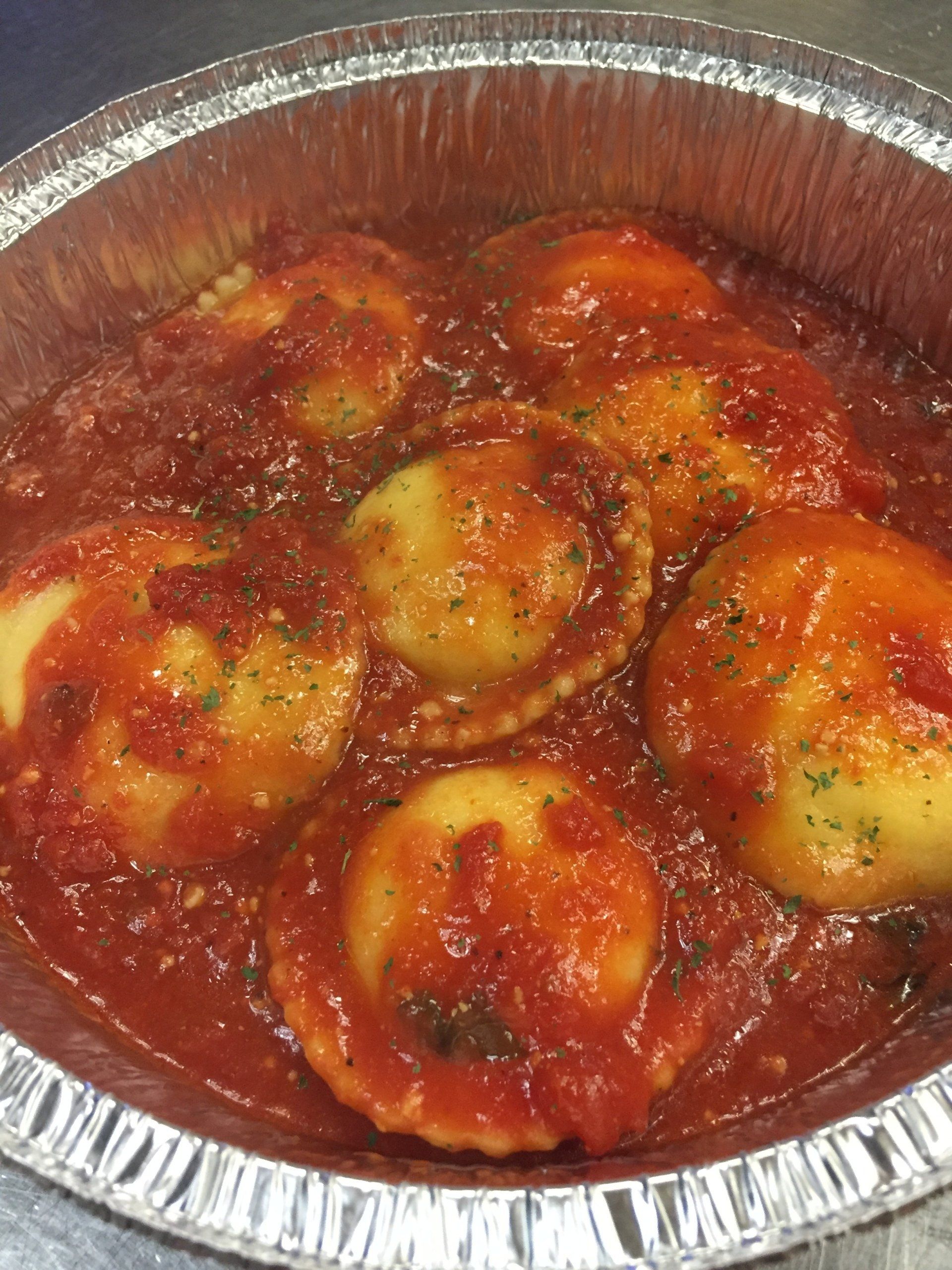 A tin foil pan filled with ravioli in tomato sauce.