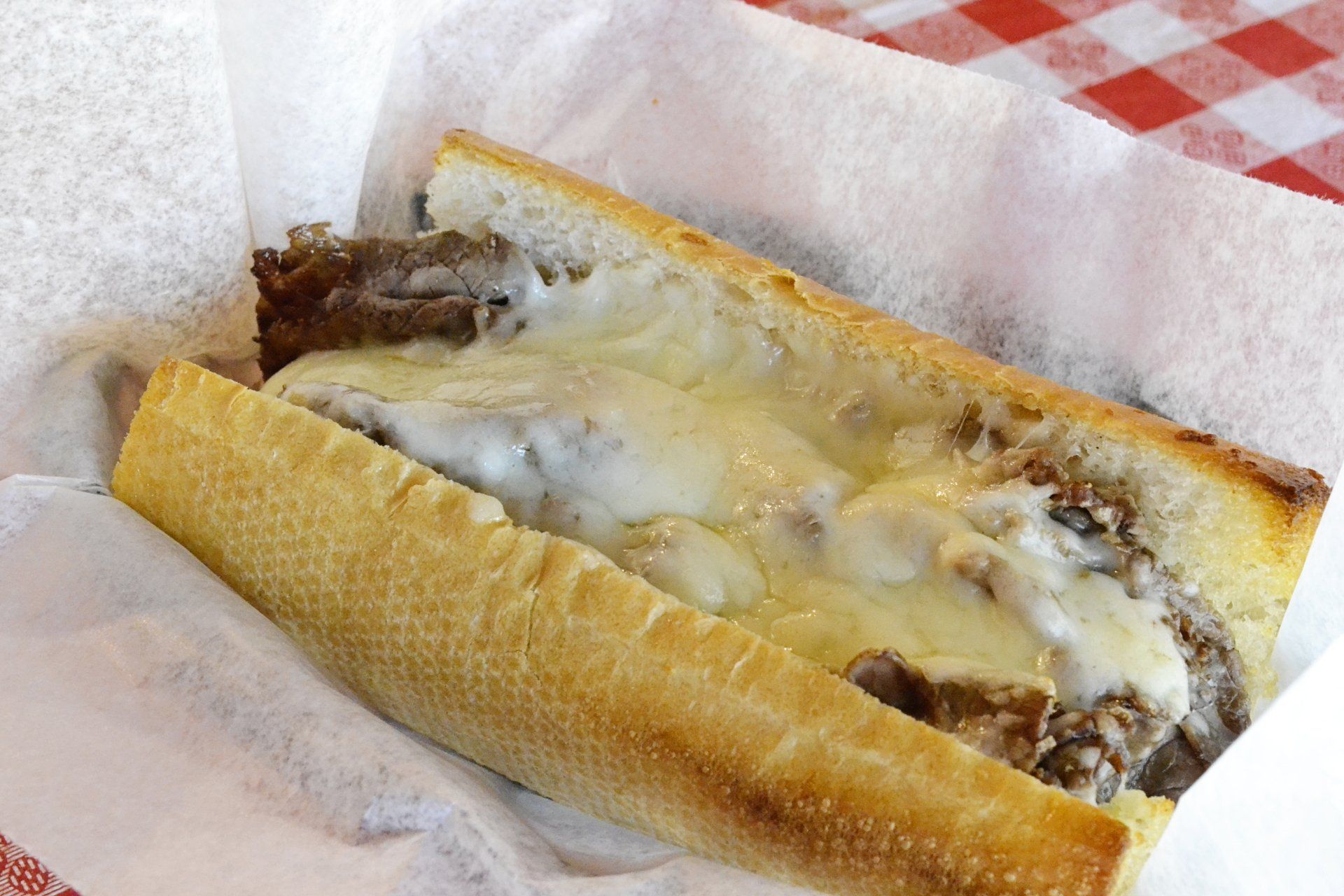 A steak and cheese sub sandwich is sitting on a napkin on a table.
