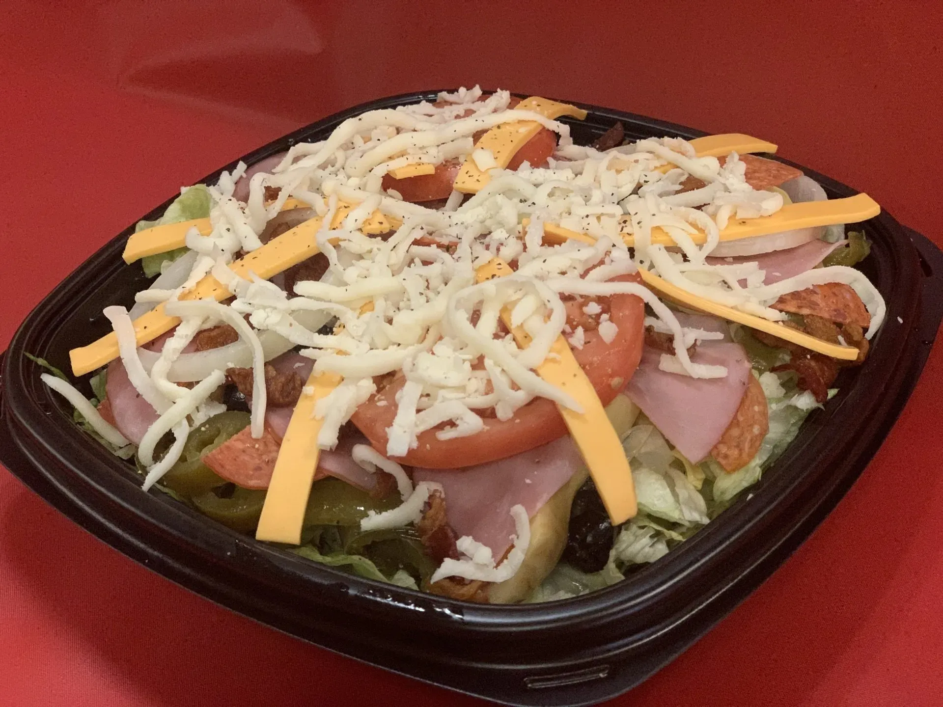 A salad in a plastic container with cheese on top