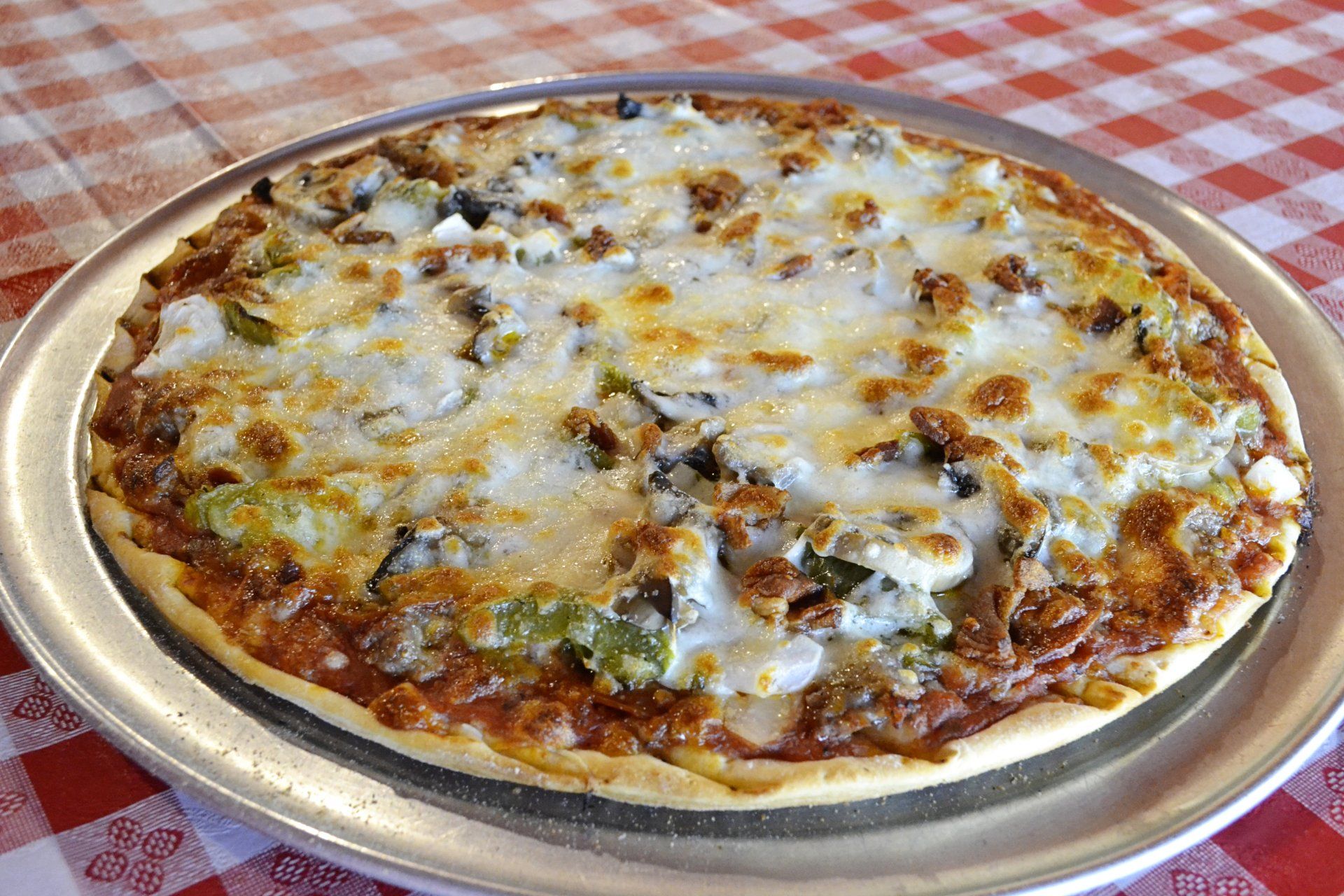 A pizza is sitting on a metal pan on a checkered table cloth.