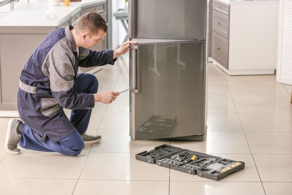 Man in Blue Jumpsuit Kneels, Repairing a Gray Refrigerator — SealTite in Tweed Heads, NSW