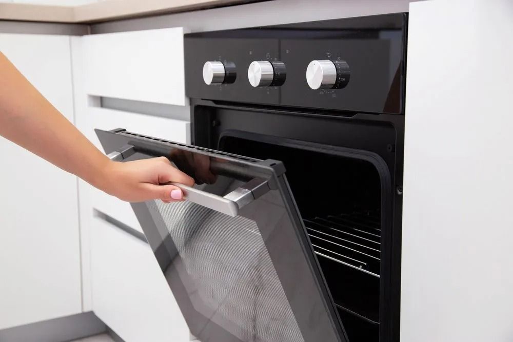 Hand Opening a Black Oven Door in a White Kitchen, the Oven is Empty With a Wire Rack — SealTite in Lismore, NSW