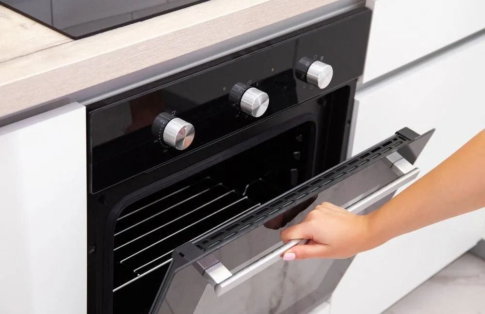 Hand Opening a Modern Oven Door in a White Kitchen, the Oven is Black With Silver Knobs — SealTite in Lismore, NSW