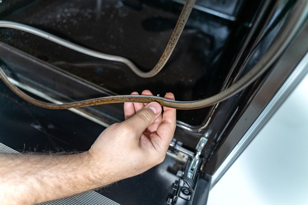 Hand Holding a Damaged Oven Door Seal Inside a Black Oven Interior — SealTite in Kingscliff, NSW