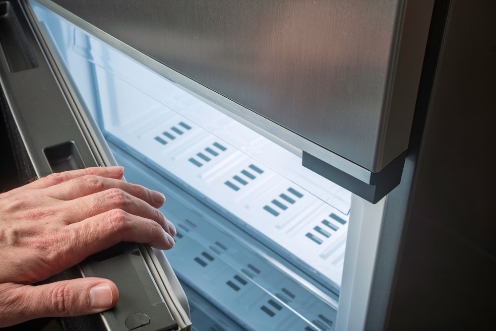 Hand Opening a Stainless Steel Refrigerator Door, Revealing Lit Shelves With Objects Inside — SealTite in Terranora, NSW