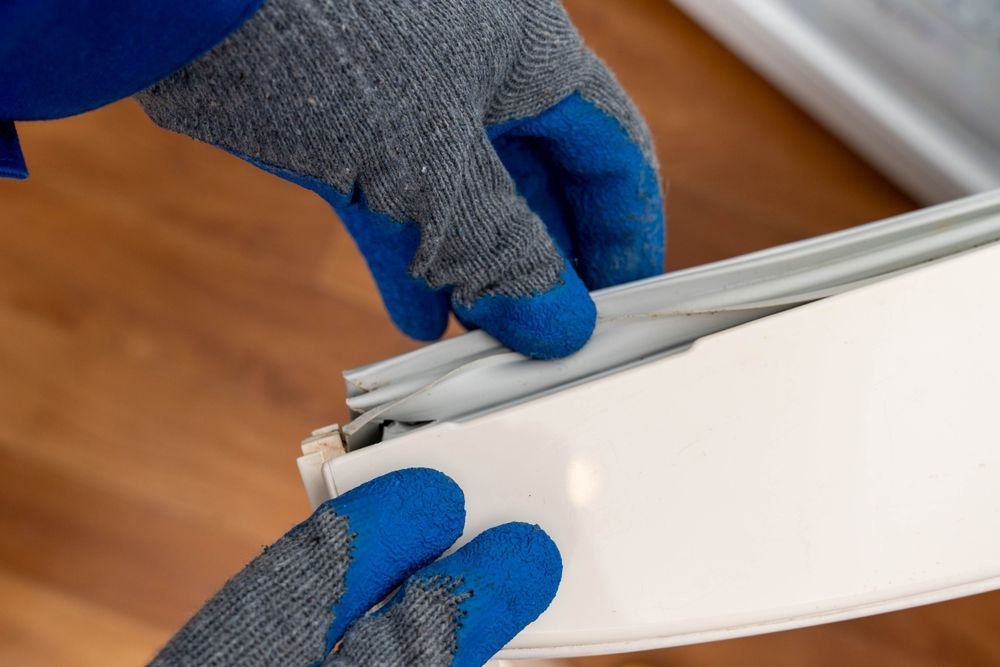 Hands in Blue Gloves Installing a White Weather Strip Into a Window Frame — SealTite in Lismore, NSW