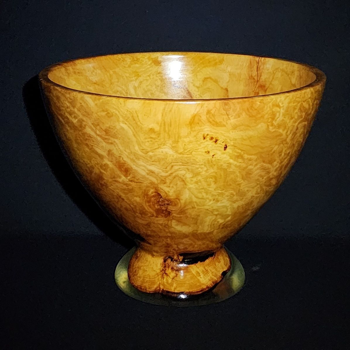 Wooden bowl with a flared shape, sitting on a clear resin base; gold and brown tones on black background.