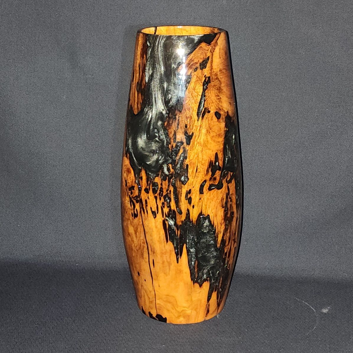 Wooden vase with orange and black patterns against a dark gray background.